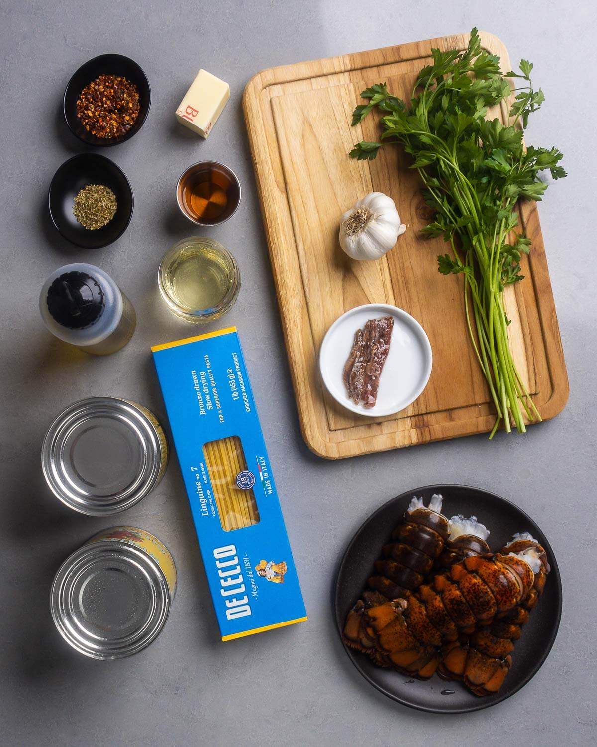 Ingredients shown: hot red pepper flakes, oregano, butter, brandy, wine, olive oil, garlic, parsley, anchovies, plum tomatoes, linguine, and lobster tails.