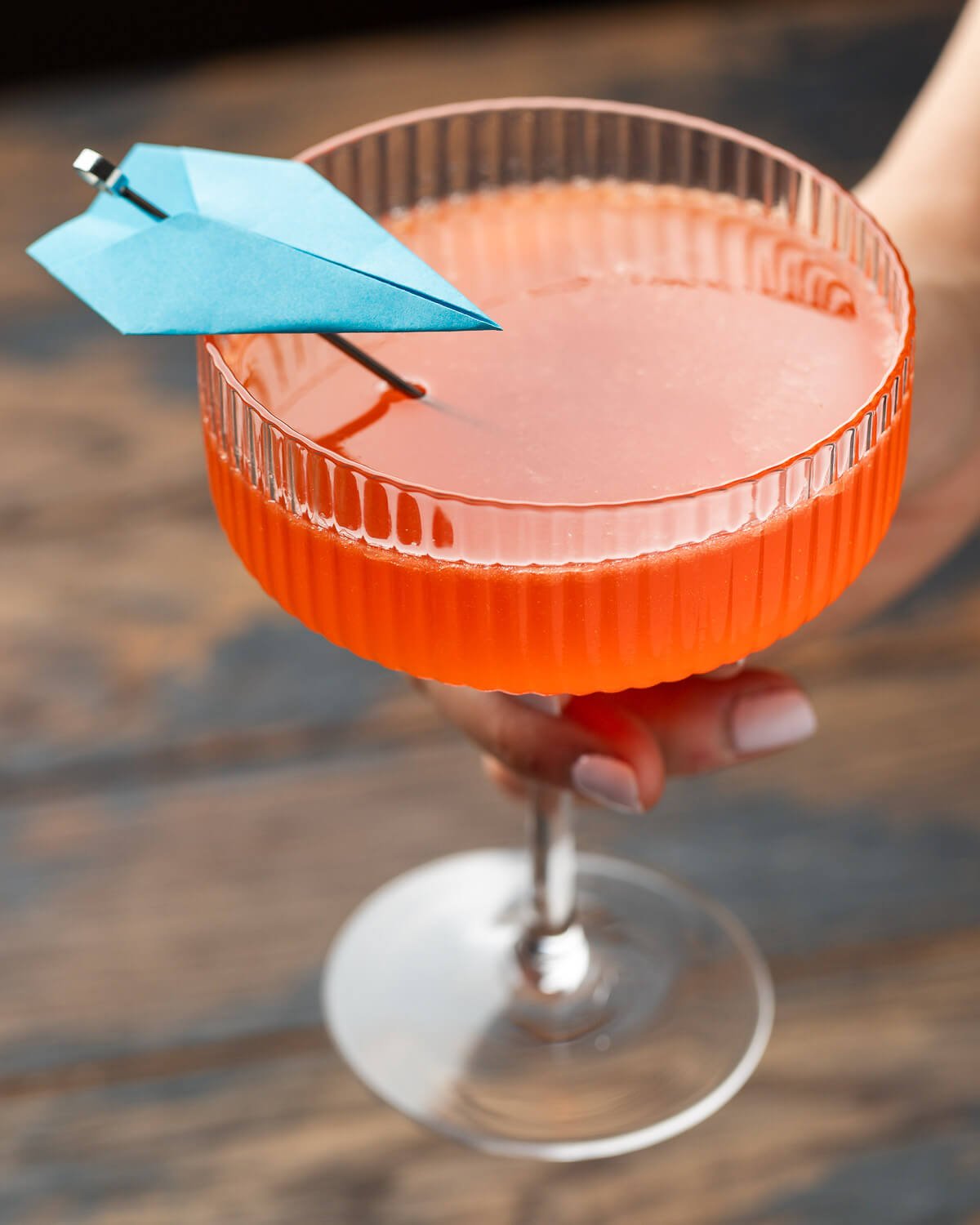 Large coupe glass held in hands with paper plane cocktail.