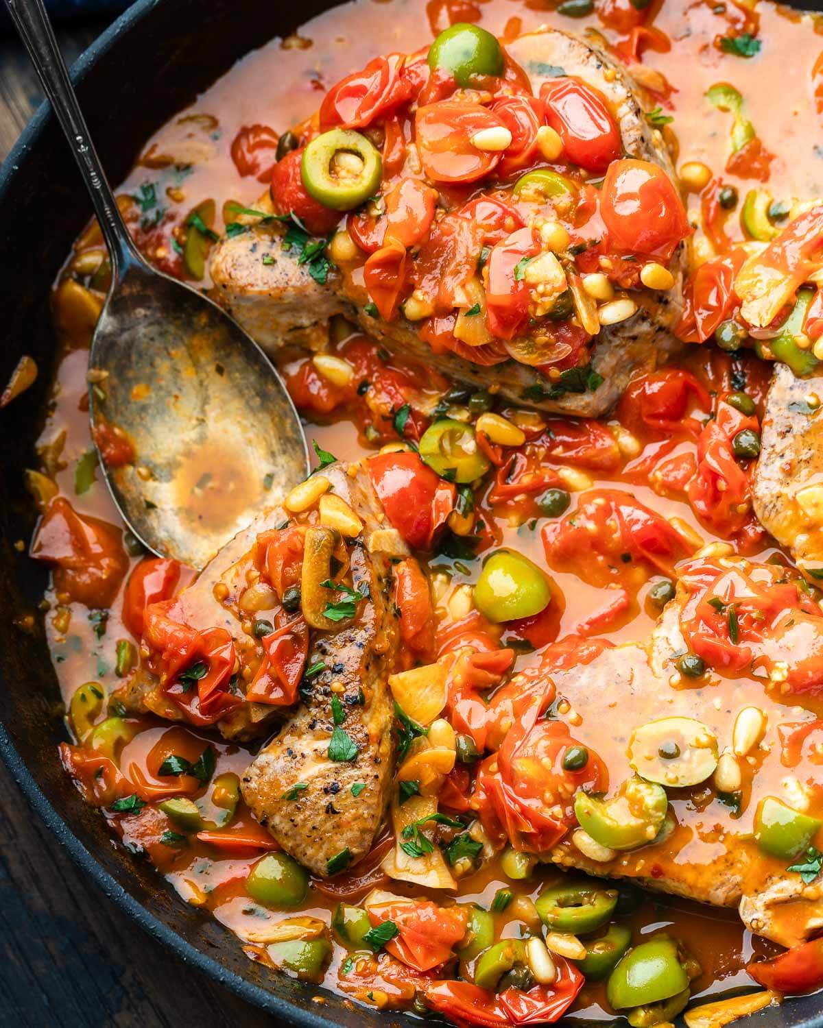 Black pan with Sicilian-style tuna smothered in olive, garlic, tomato, and pine nut sauce.
