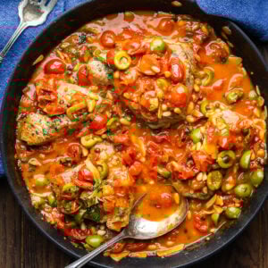 Overhead shot of large black pan with Sicilian-style tuna steaks covered in olive tomato sauce.