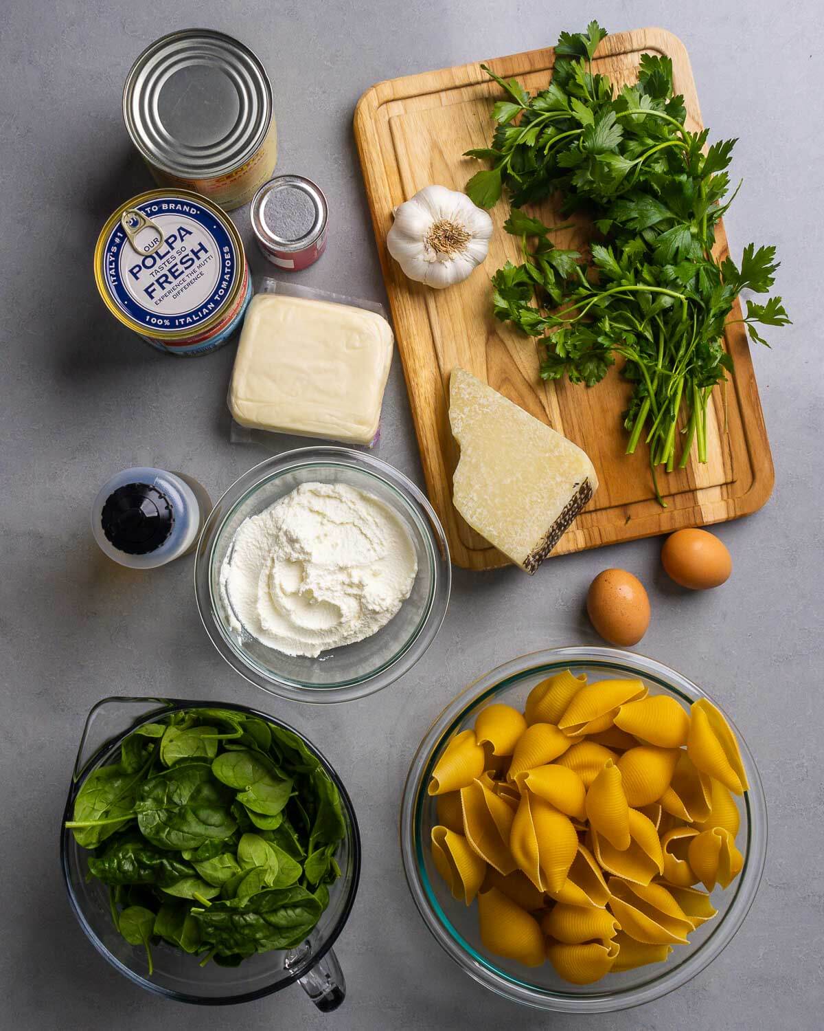 Ingredienets shown: canned tomatoes and paste, garlic, parsley, Pecorino, mozzarella, ricotta, olive oil, eggs, spinach, and large pasta shells.