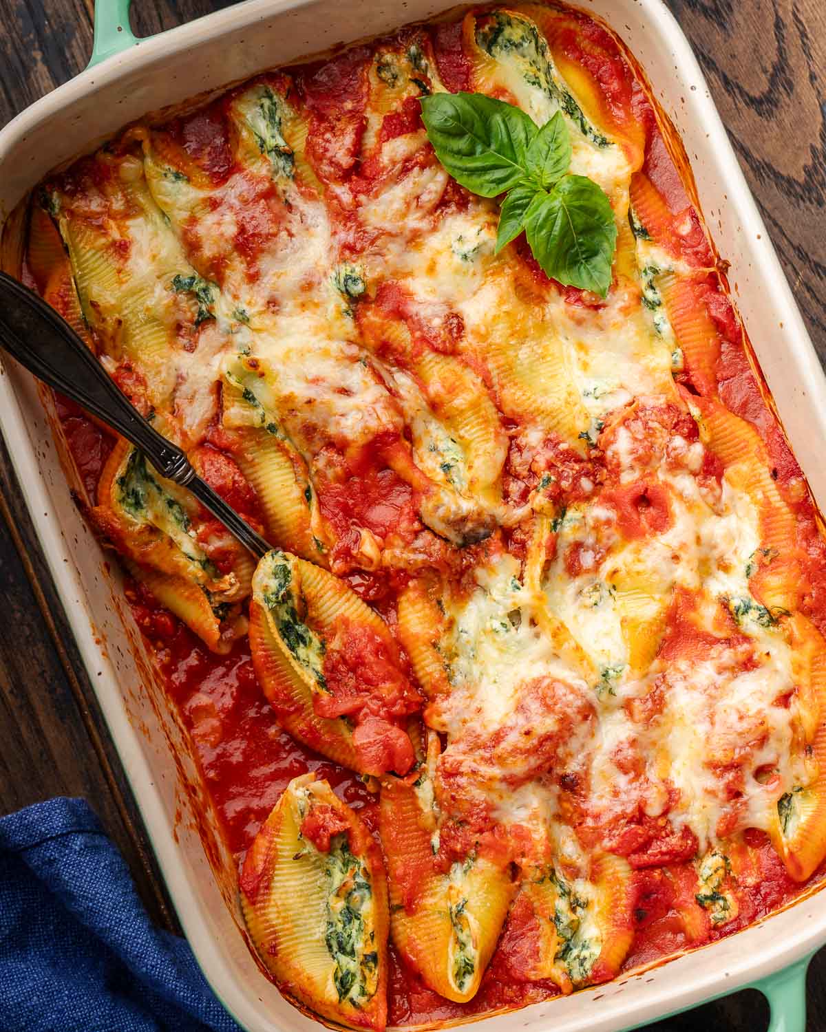 Large baking dish filled with spinach ricotta stuffed shells with basil garnish.