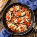 Chicken sorrentino in black pan with blue napkins and loaf of bread.
