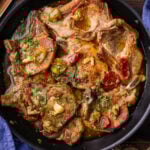 Pork chops with vinegar peppers in black pan.