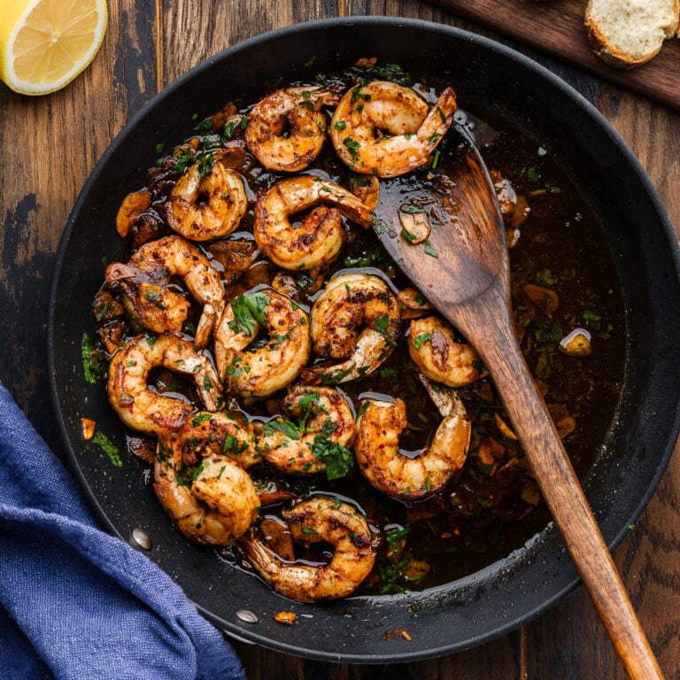 Gambas al ajillo in black pan with wooden spoon.