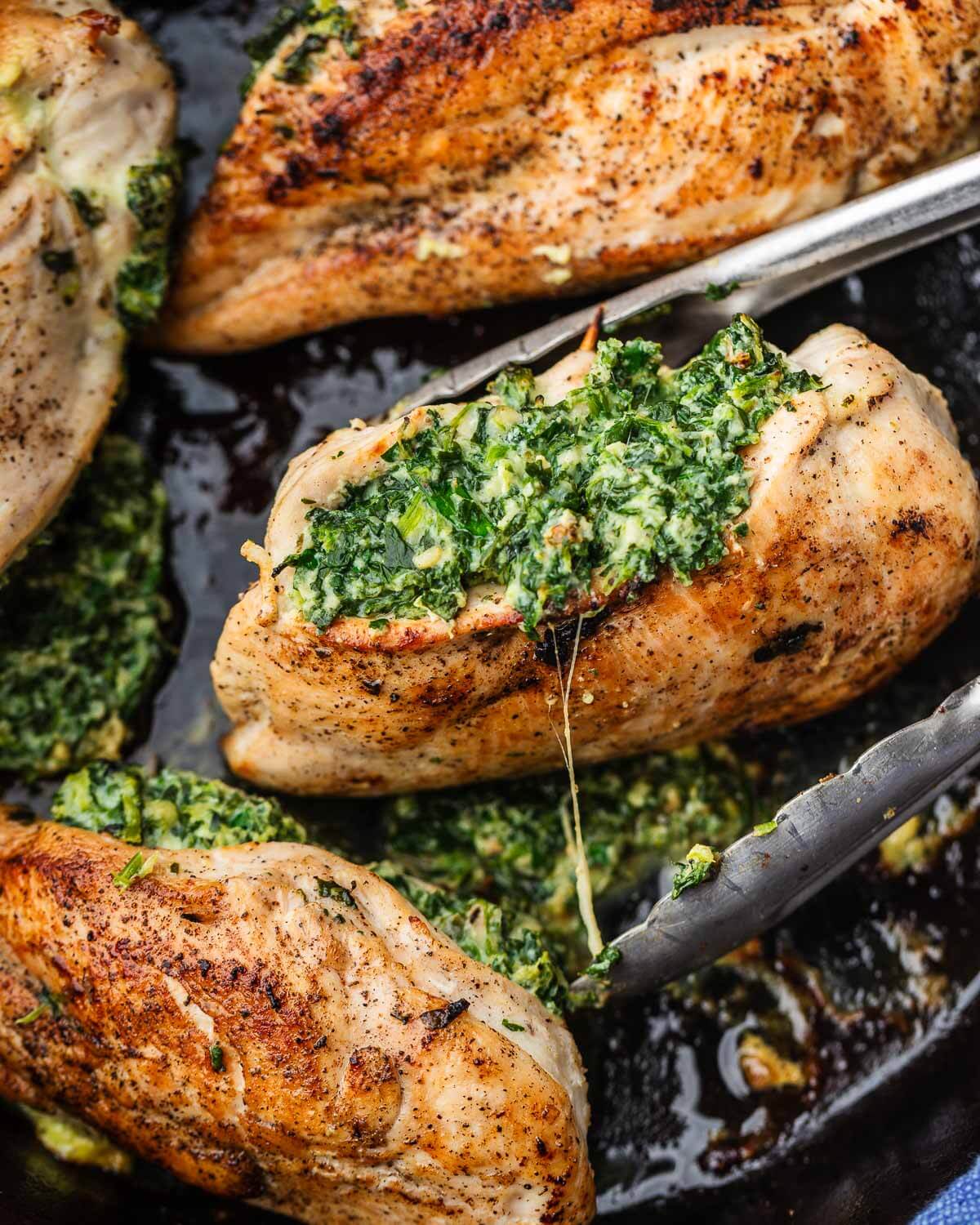 Tongs wrapped around a cooked spinach and cheese stuffed chicken breast.