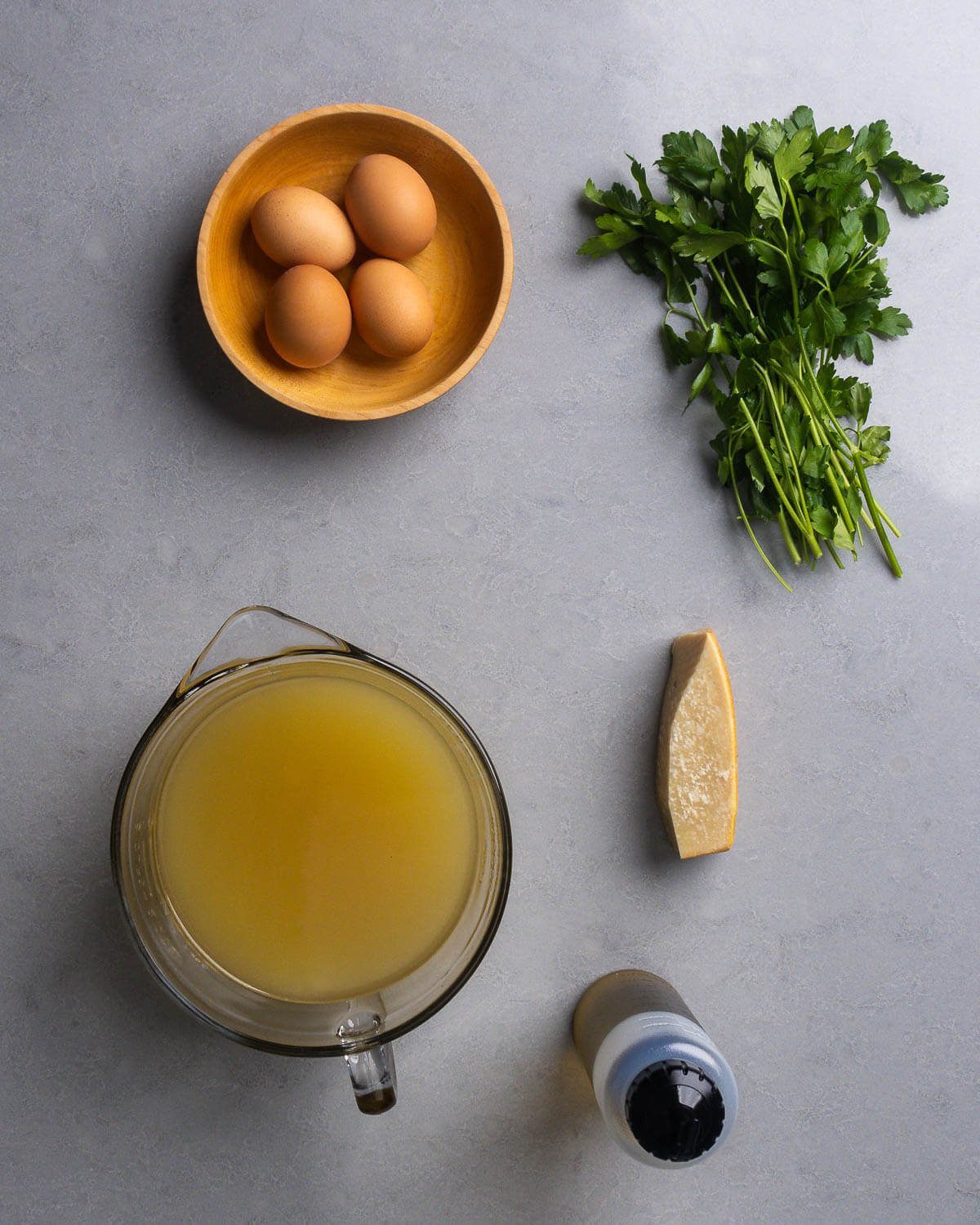 Ingredients shown: eggs, parsley, chicken stock, block of Parmigiano Reggiano, and extra virgin olive oil.