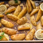 Greek potatoes in large baking pan with lemon and parsley garnish.