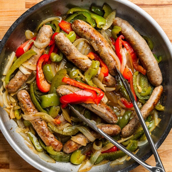 Sausage and peppers in pan with tongs.
