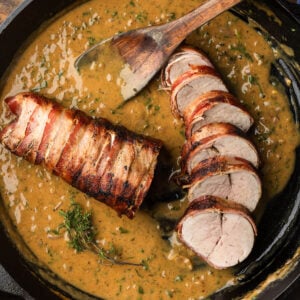 Sliced bacon wrapped pork tenderloin with creamy mustard sauce in cast iron pan.