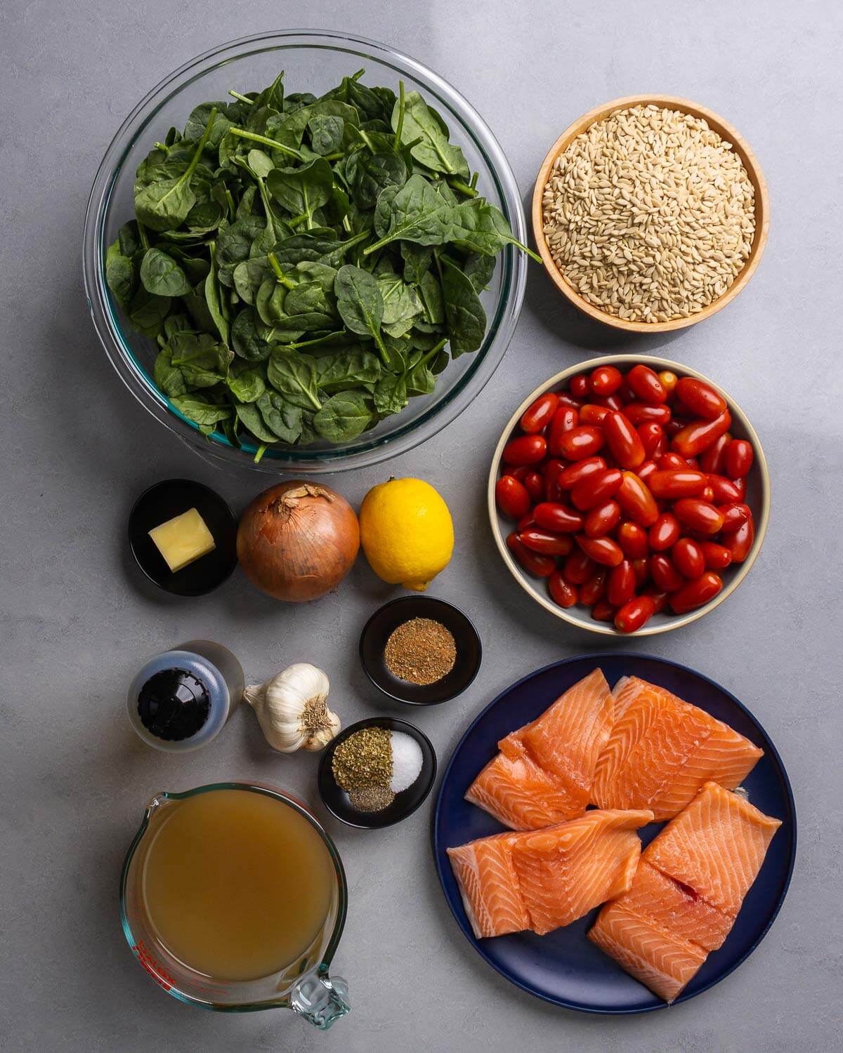 Ingredients shown: spinach, orzo, butter, onion, lemon, cherry tomatoes, Cajun spice, olive oil, garlic, seasonings, chicken stock, and salmon filets.