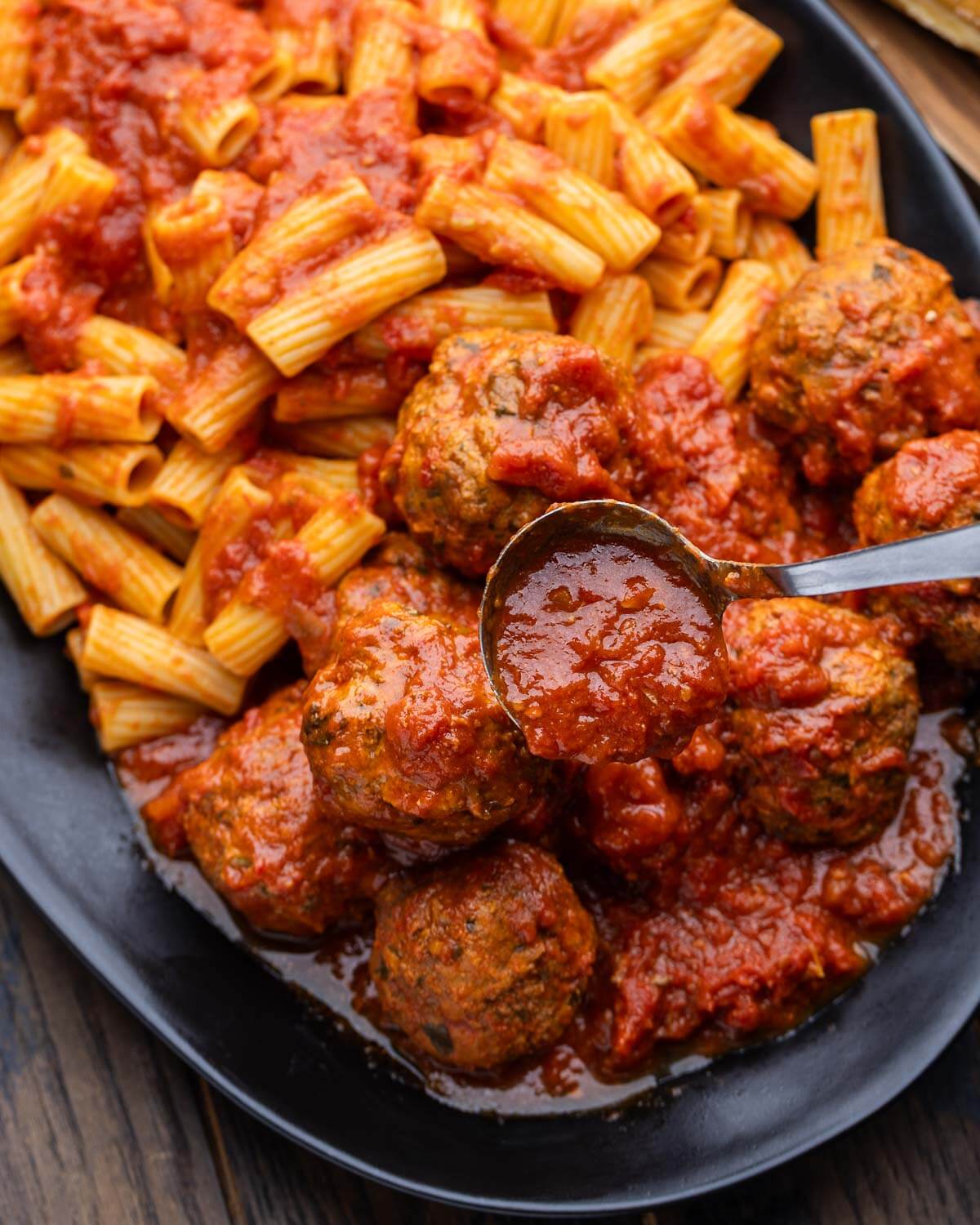 Ladle pouring sauce over the cooked meatballs and rigatoni pasta.