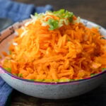 Carrot salad in white bowl topped with green onion.