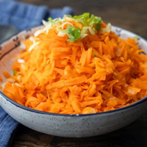 Carrot salad in white bowl topped with green onion.