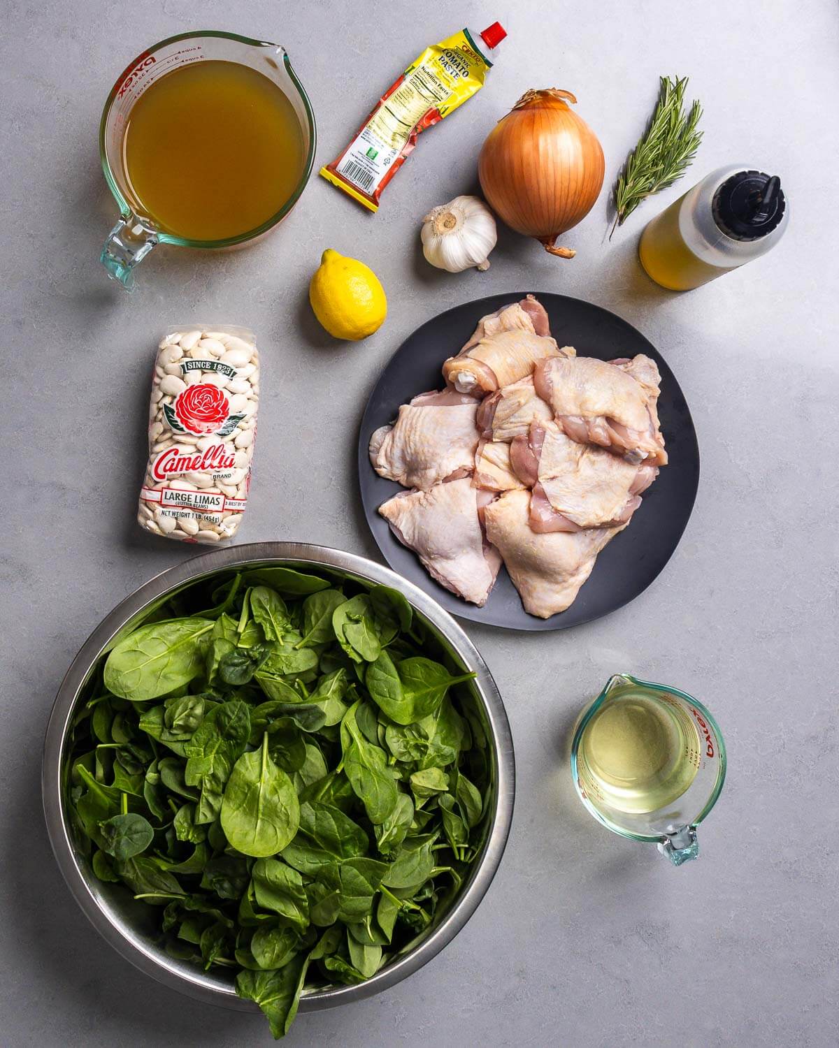 Ingredients shown: chicken stock, tomato paste, lemon, garlic, onion, rosemary, olive oil, beans, chicken thighs, spinach, and white wine.