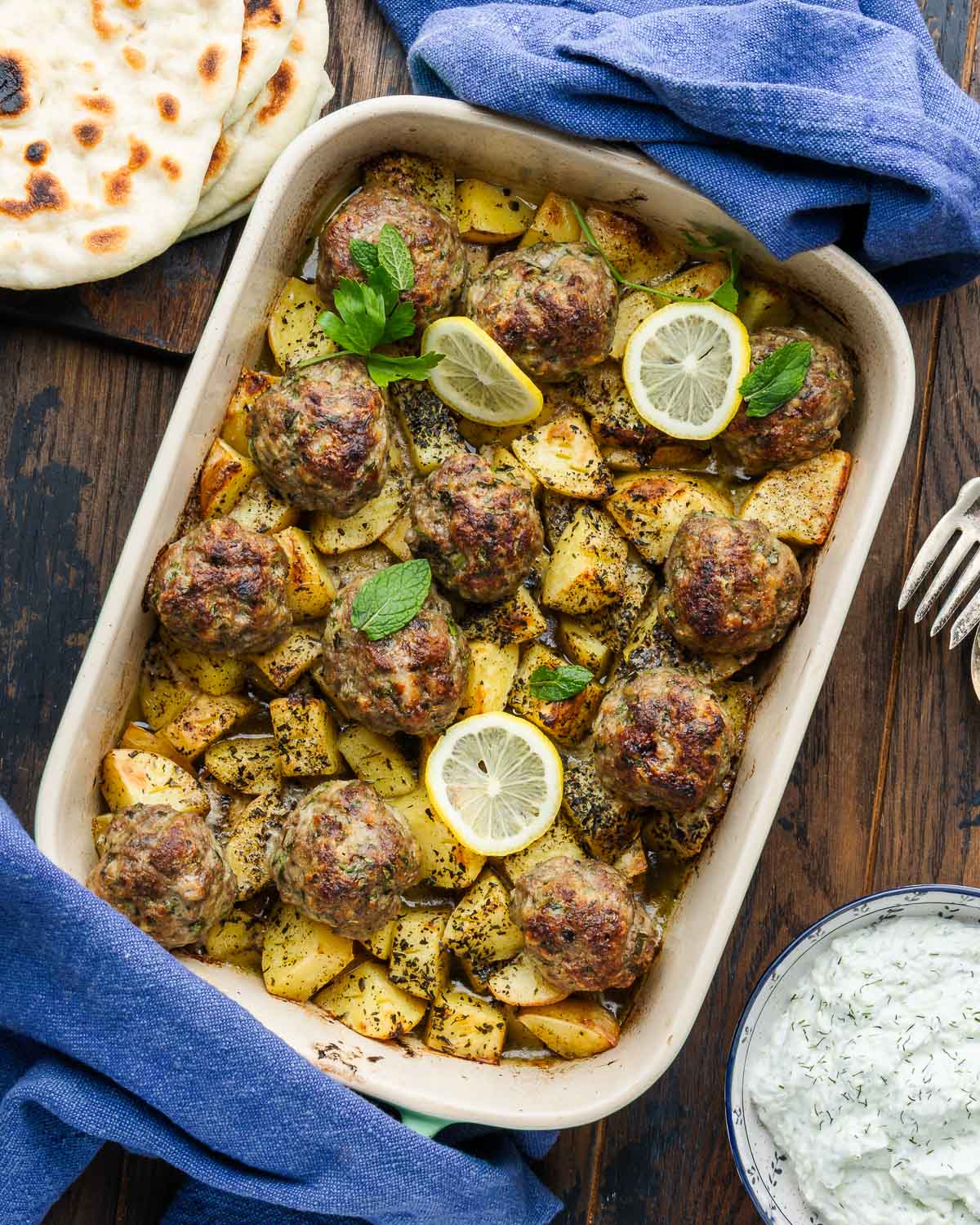 Greek meatballs and potatoes in baking dish with pita and tzatzki sauce on the side.