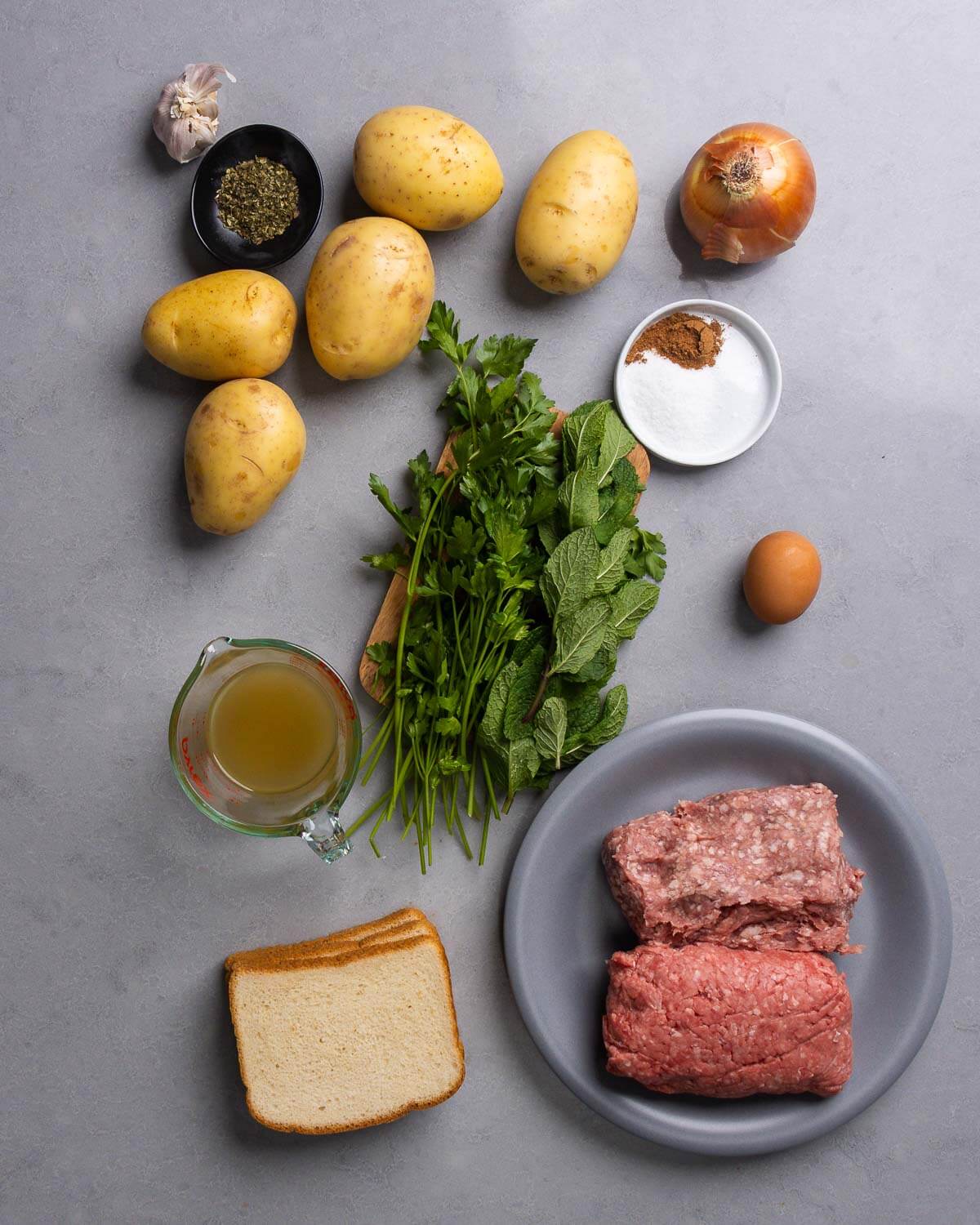 Ingredients shown: garlic, oregano, potatoes, onion, nutmeg,salt, parsley, mint, egg, chicken stock, white bread, ground chuck, and ground lamb.