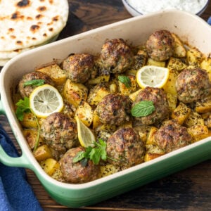 Greek meatballs and potatoes in baking dish with pita and tzatzki sauce on the side.