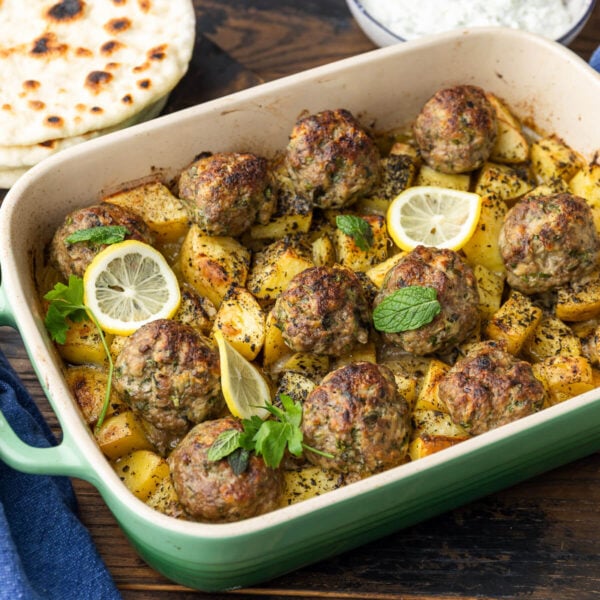 Greek meatballs and potatoes in baking dish with pita and tzatzki sauce on the side.