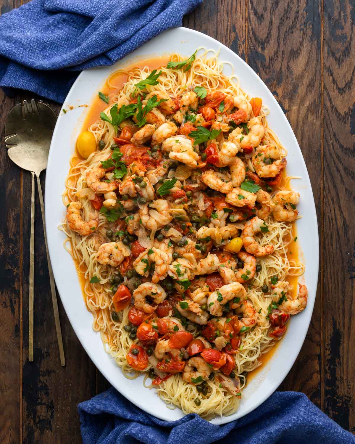 Old Bay shrimp with capellini in white platter with blue napkins and serving spoons.