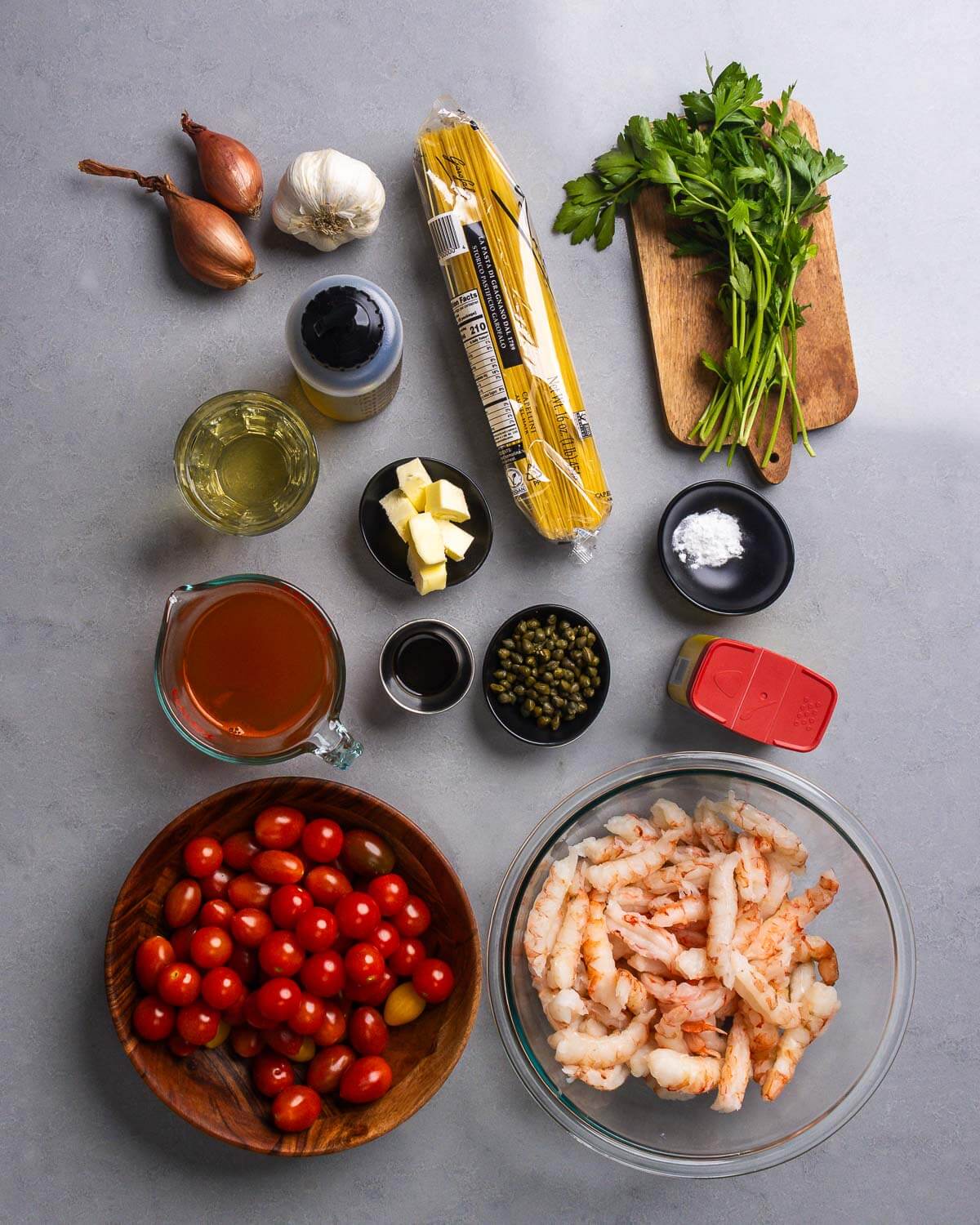 Ingredients shown: shallots, garlic, capellini pasta, parsley, wine, butter, lobster stock, worcestershire sauce, capers, baking soda, Old Bay seasoning, cherry tomatoes, and shrimp.