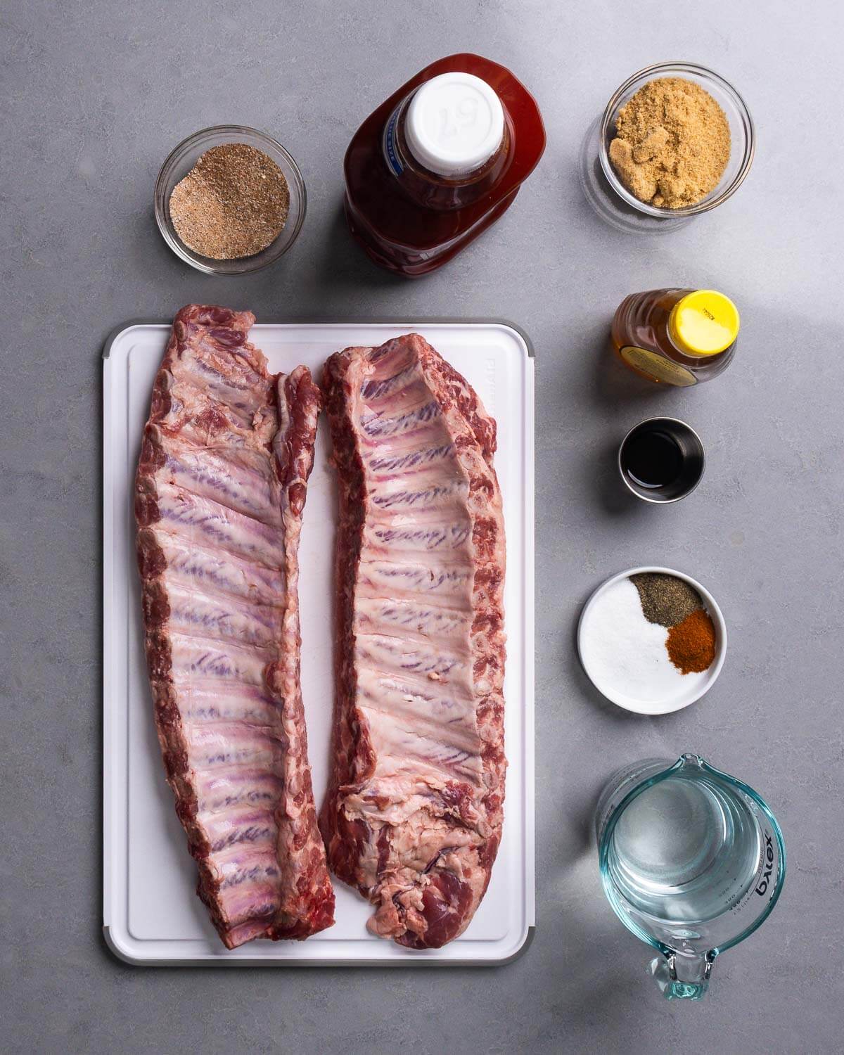 Ingredients shown: spice rub mixture, ketchup, brown sugar, honey, worcestershire sauce, spices, vinegar, and two racks of baby back ribs.