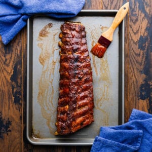 Rack of oven bbq ribs in sheet pan with brush covered with bbq sauce.