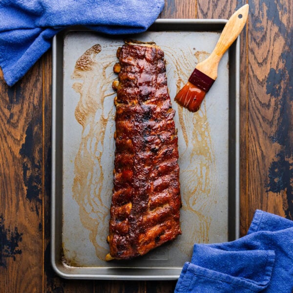 Rack of oven bbq ribs in sheet pan with brush covered with bbq sauce.