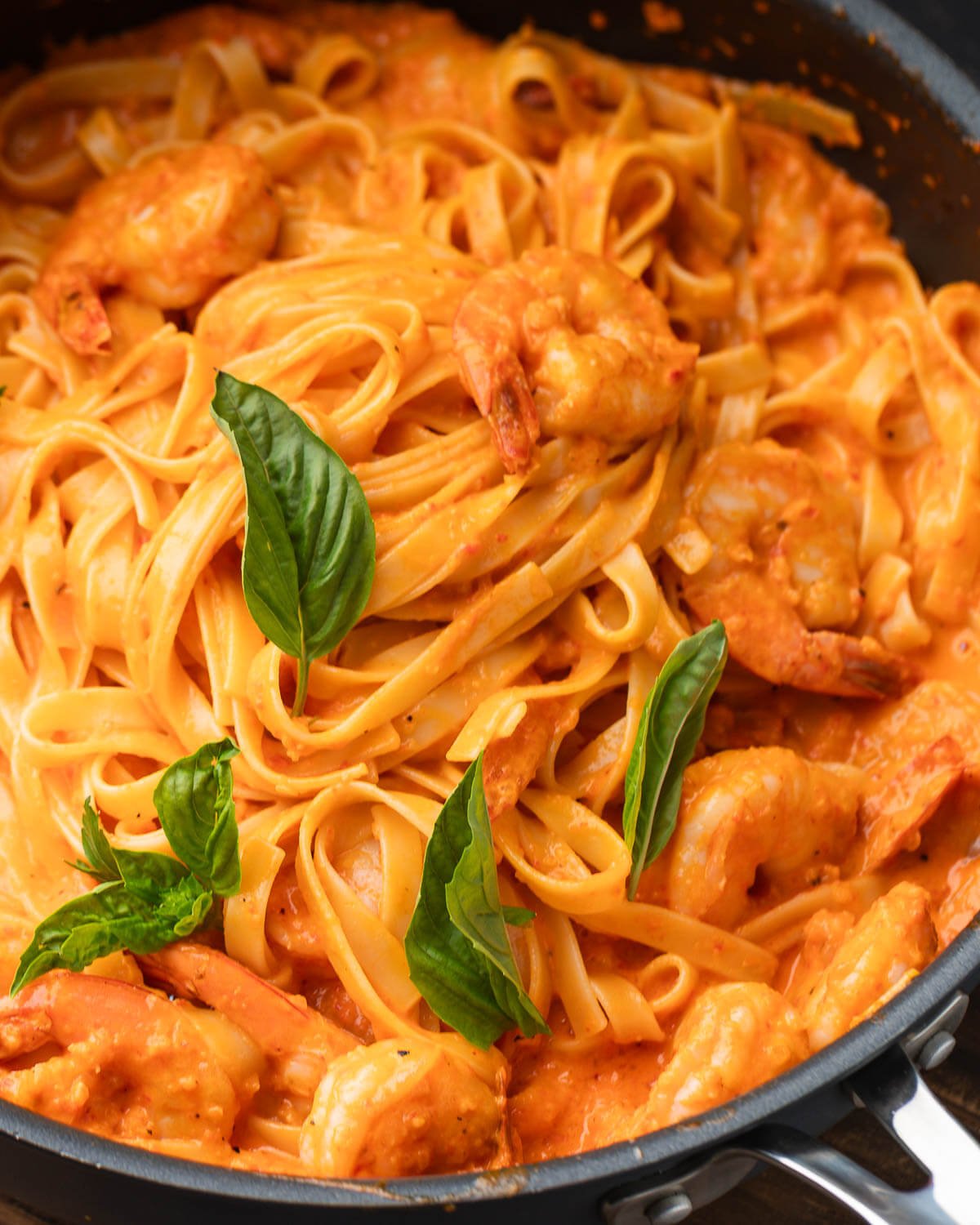 Roasted red pepper pasta with shrimp in black pan with basil leaves.