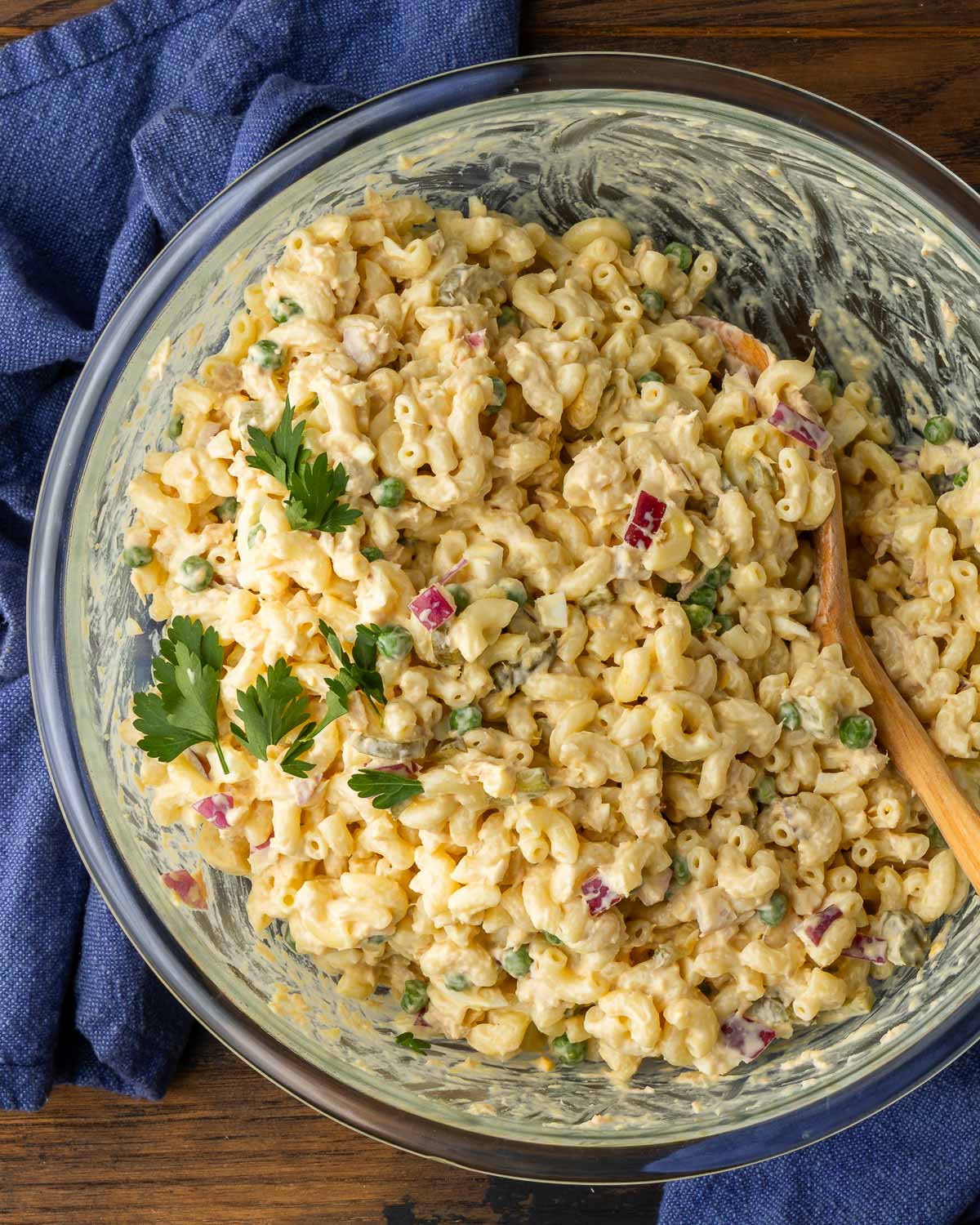 Tuna macaroni salad in glass bowl with blue napkins on the side.