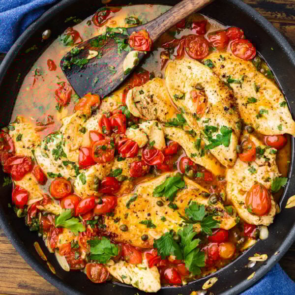 Large black pan of chicken with capers and tomatoes.