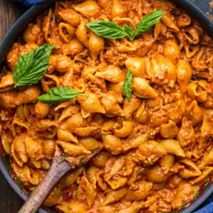 Creamy beef and shells pasta in large black pan with basil garnish.