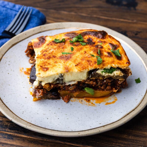 Large slice of moussaka on white and gold plate.