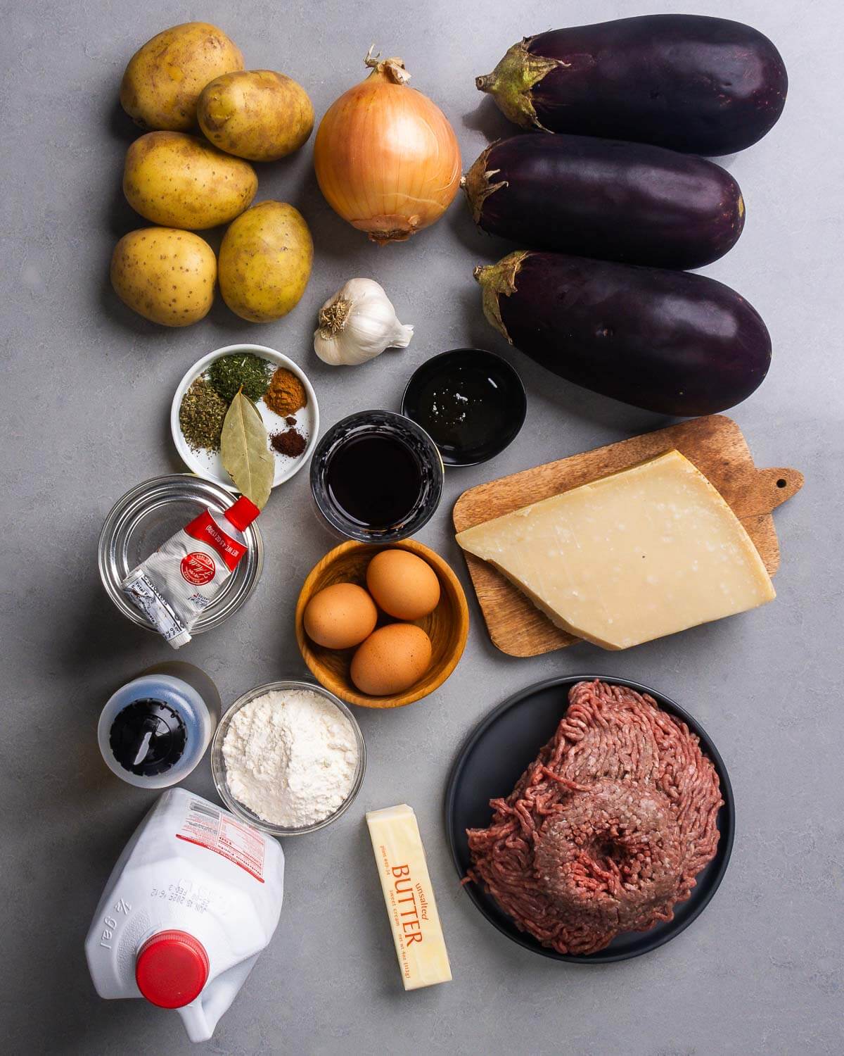 Recipe ingredients shown: potatoes, onion, eggplants, garlic, spices, red wine, tomato paste, eggs, parmesan cheese, olive oil, flour, milk, butter, and ground beef.