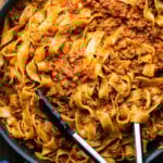 Pappardelle Bolognese in large pan with tongs.