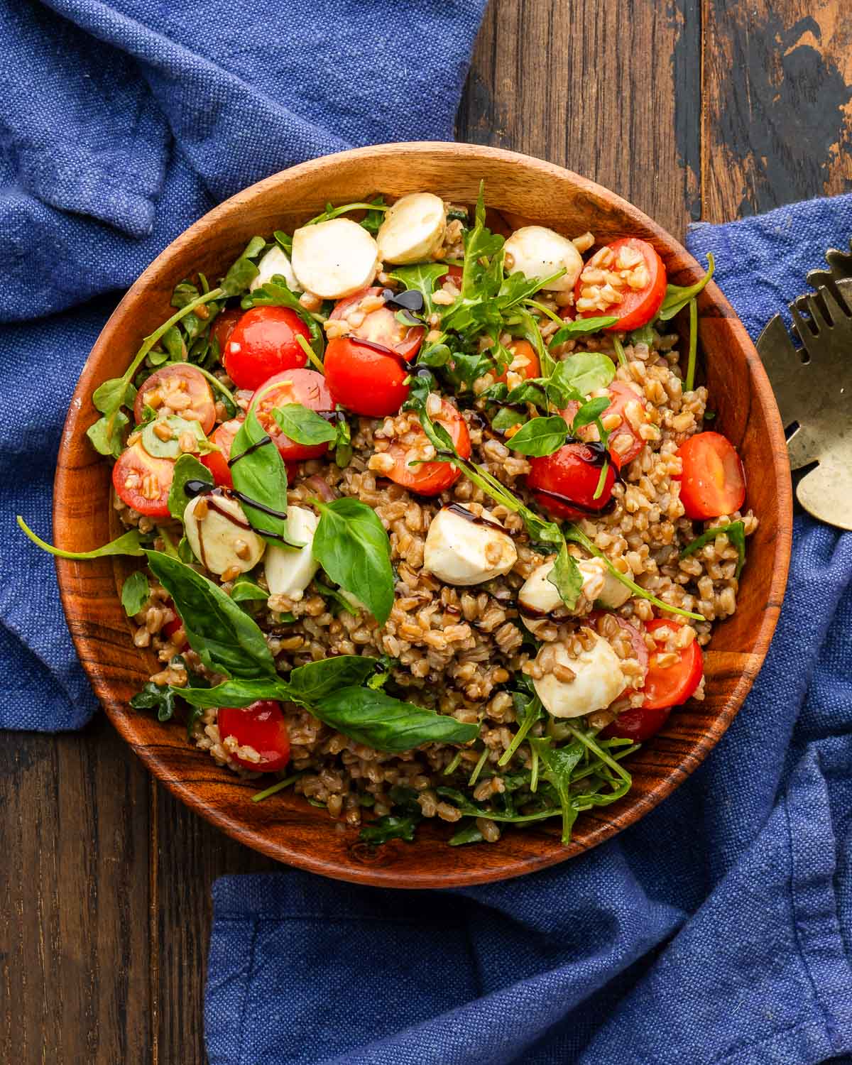 Caprese farro salad in wood bowl with blue napkins.