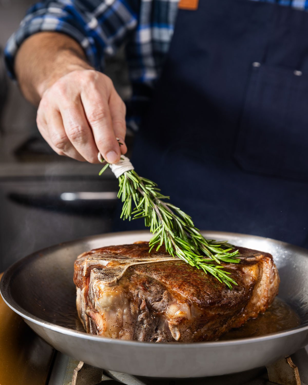 Basting a large porterhouse with rosemary and olive oil.