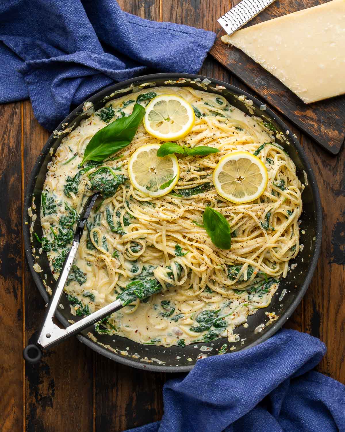 Lemon ricotta spinach pasta in large black pan with blue napkins and block of parmesan cheese.