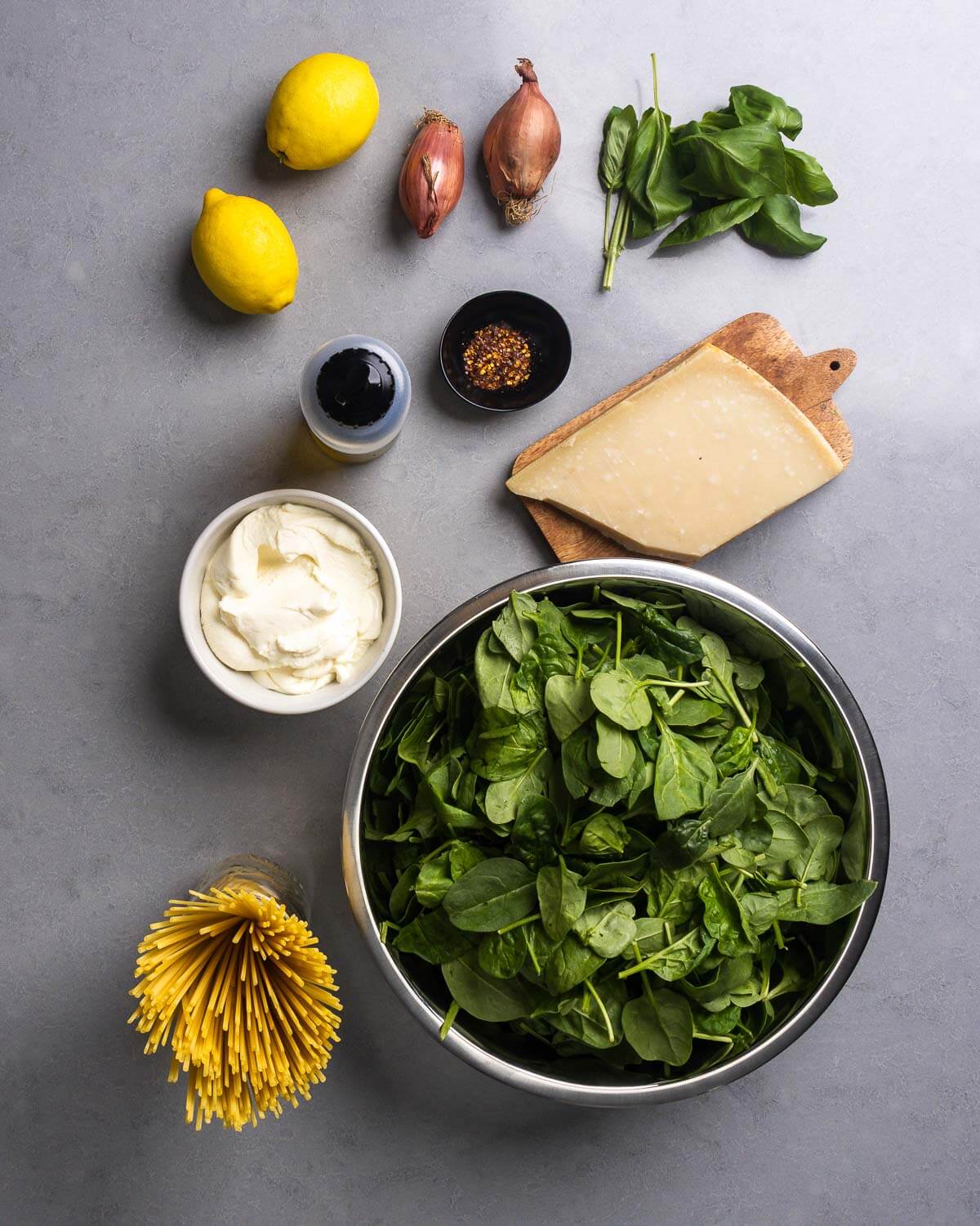 Ingredients shown: lemons, shallots, basil, olive oil, chili flakes, parmesan block, ricotta, linguine, and baby spinach.