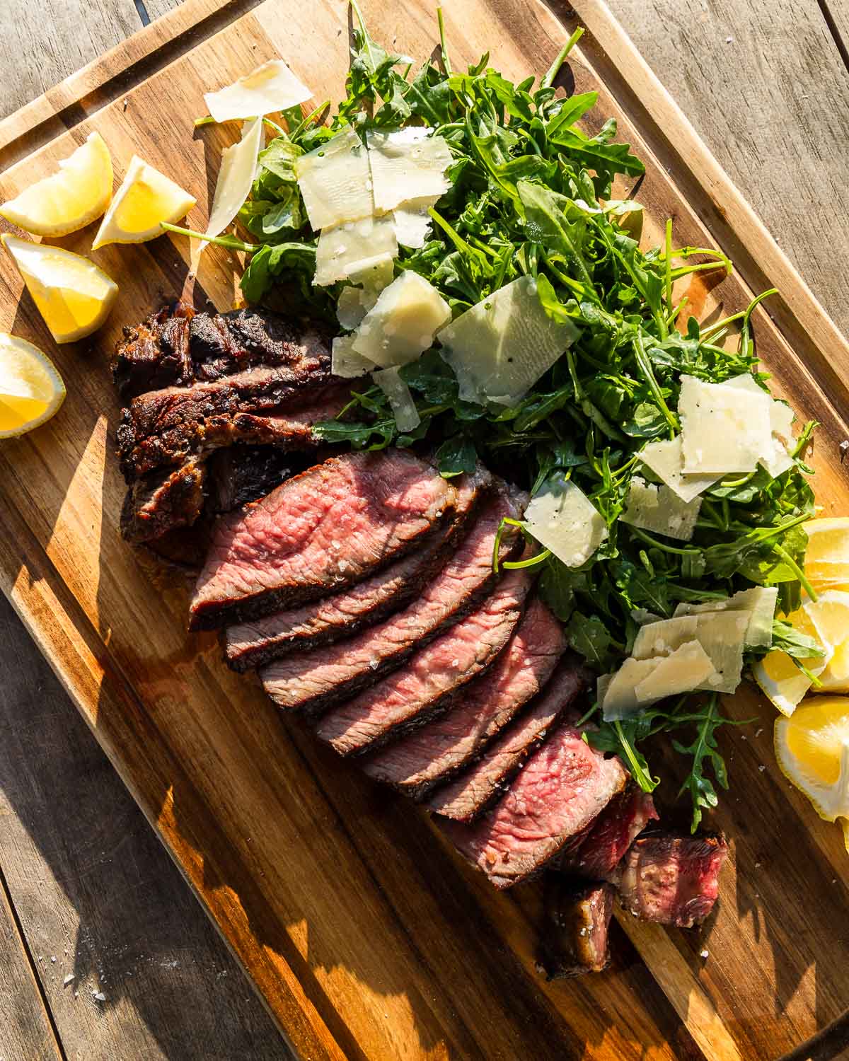 Steak Tagliata on wooden cutting board with lemon wedges on the side.