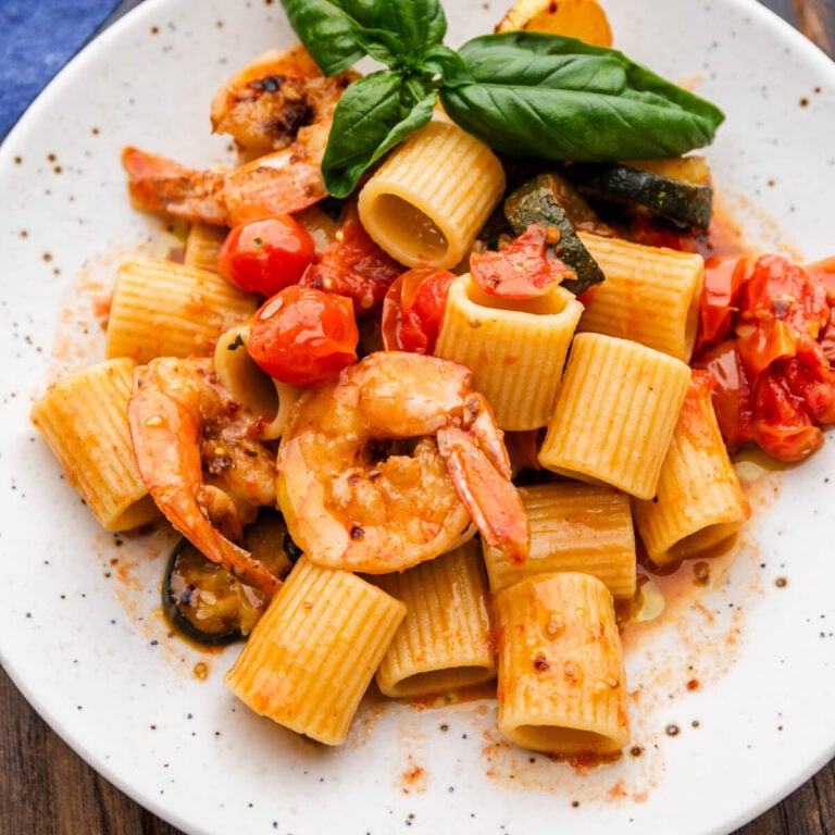 Zucchini tomato shrimp pasta on white plate.