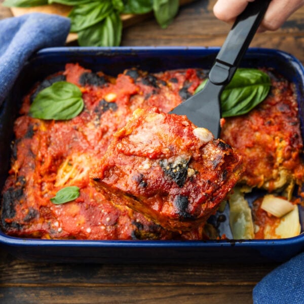 Slice of artichoke parmesan held over baking dish.