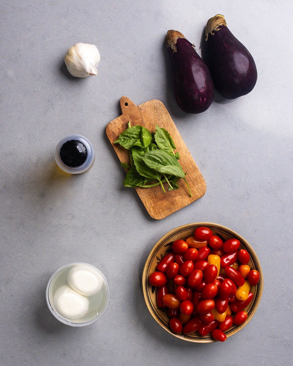 Ingredients shown: garlic, eggplant, olive oil, basil, burrata, and cherry/grape tomatoes.