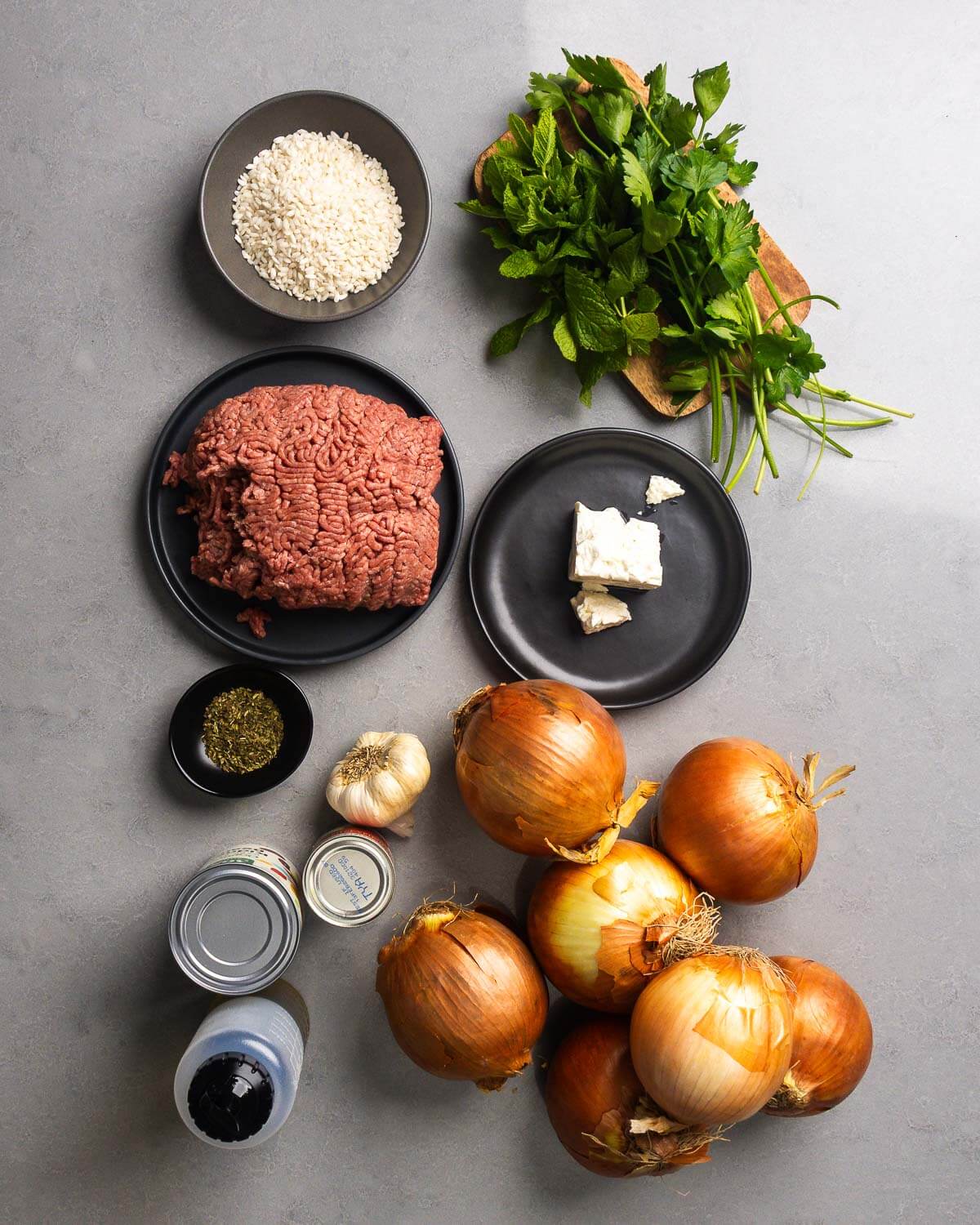 Ingredients shown: rice, mint, parsley, ground chuck, feta cheese, oregano, garlic, onions, tomato paste, crushed plum tomatoes, and olive oil.
