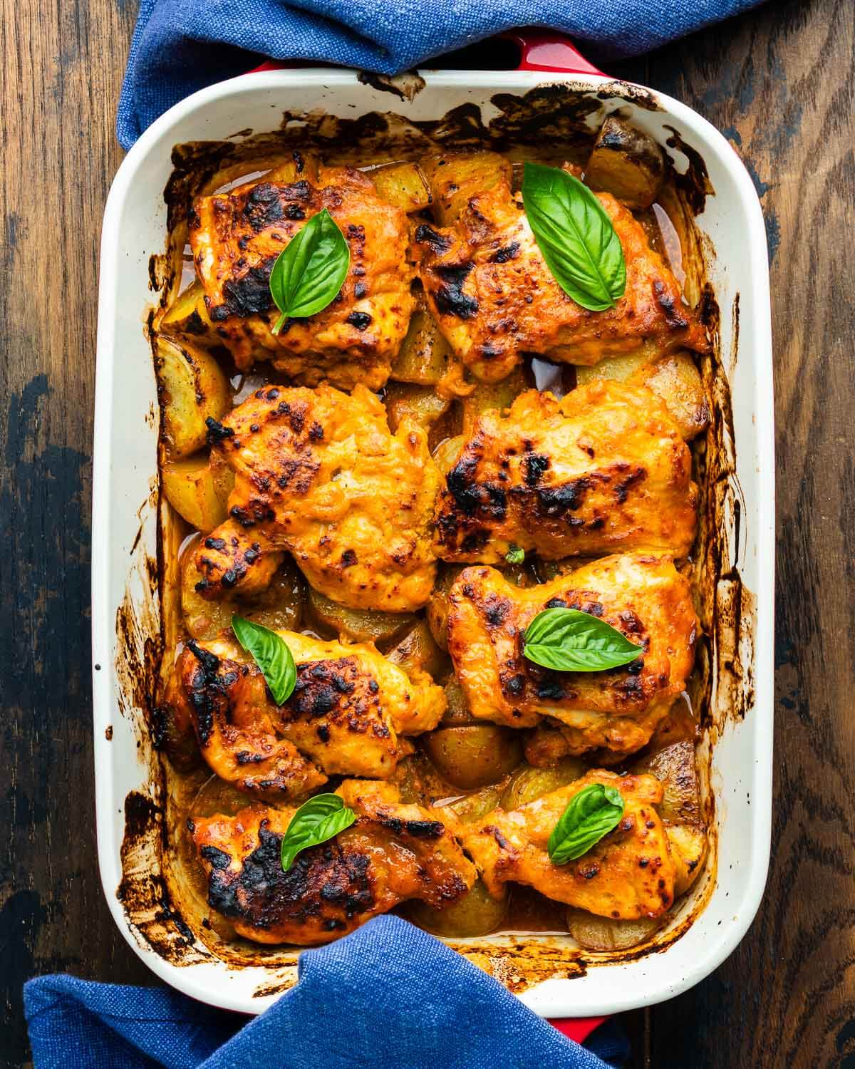 Hot honey chicken and potatoes in baking dish with basil garnish.