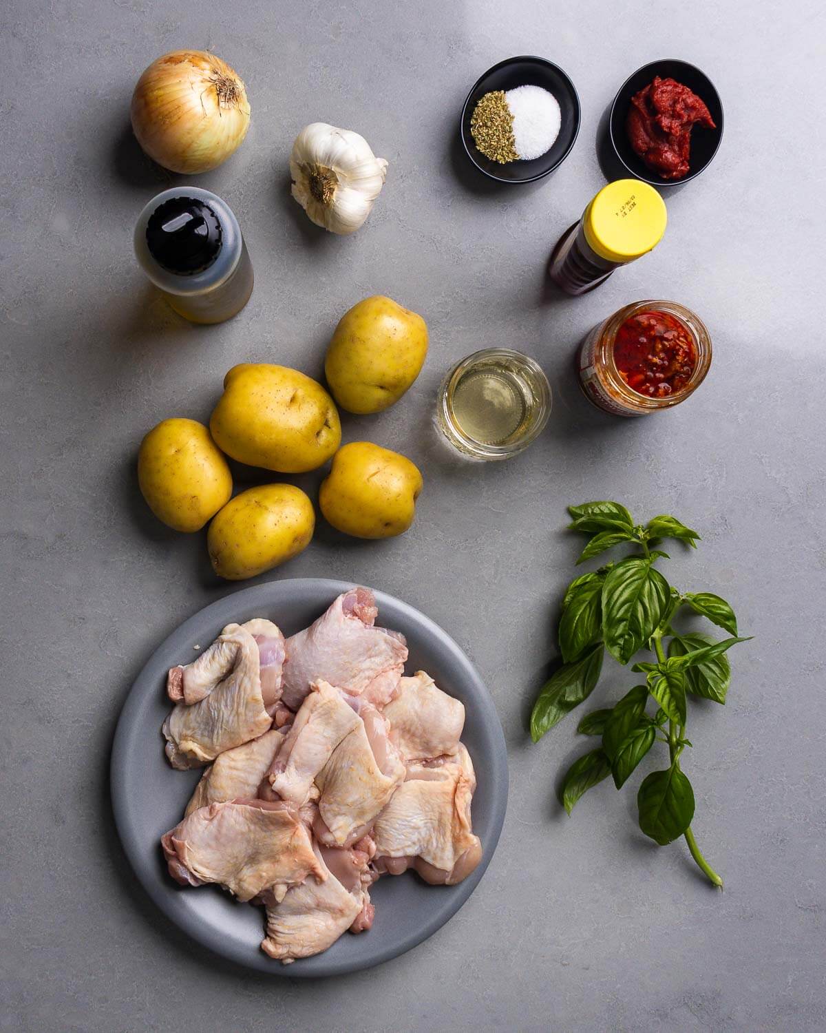 Ingredients shown: onion, olive oil, garlic, oregano, salt, tomato paste, honey, potatoes, wine, Calabrian chili paste, chicken thighs, and basil.