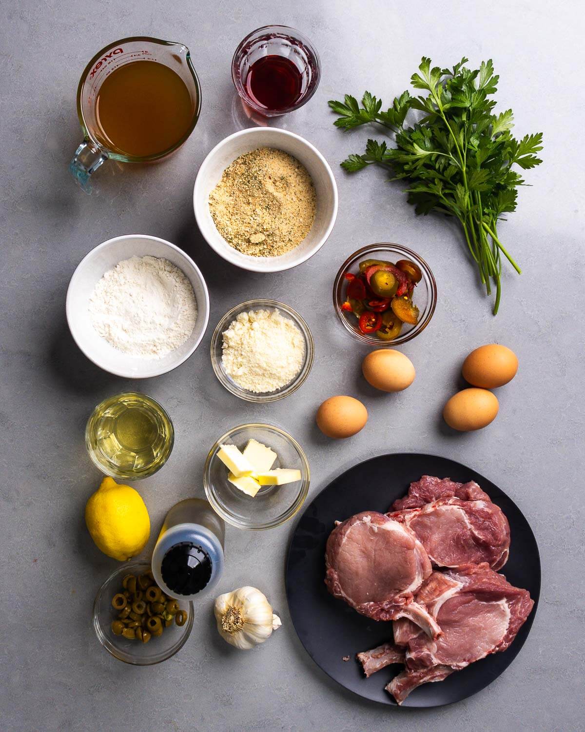 Ingredients shown: chicken stock, vinegar, parsley, flour, breadcrumbs, parmesan cheese, cherry peppers, eggs, white wine, butter, lemon, olive oil, olives, garlic, and pork chops.