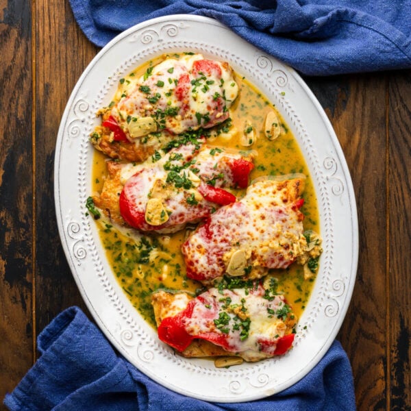Chicken with red roasted peppers and mozzarella on white platter.