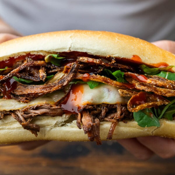 Hands holding chuck roast sandwich with crispy onions.