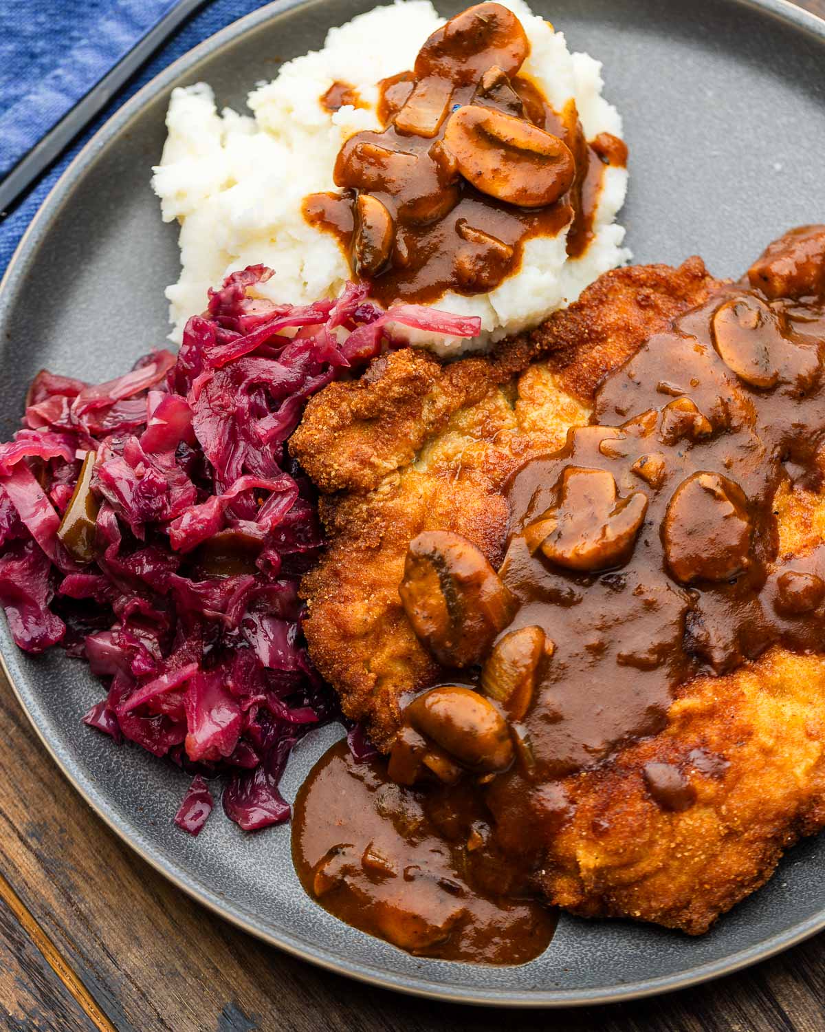 Jägerschnitzel, mashed potatoes, and red cabbage on grey plate.